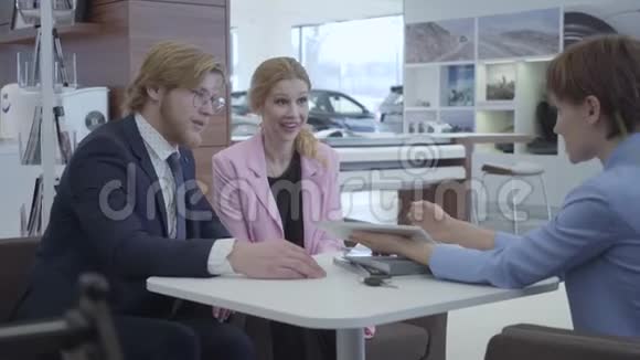 一位穿着时尚西装的汽车销售人员向年轻成功的夫妇提供了在平板电脑上选择汽车品牌的机会汽车视频的预览图