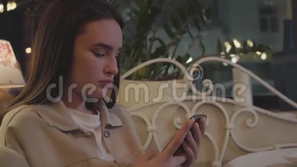 一幅可爱的年轻女孩坐在餐厅的桌子旁用手机发短信的肖像美味的蛋糕是视频的预览图
