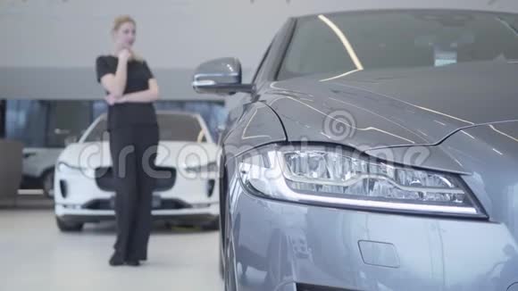 模糊的微笑的女人身材穿着黑色的衣服站在车展上环顾四周现代银色轿车的前照灯视频的预览图