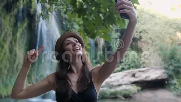 女人在国家公园瀑布附近用手机自拍笑得开心视频的预览图