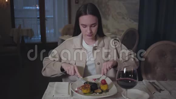 可爱的女人吃着美味的牛肉或羊肉配上烧烤玉米和西葫芦再配上一杯红酒视频的预览图