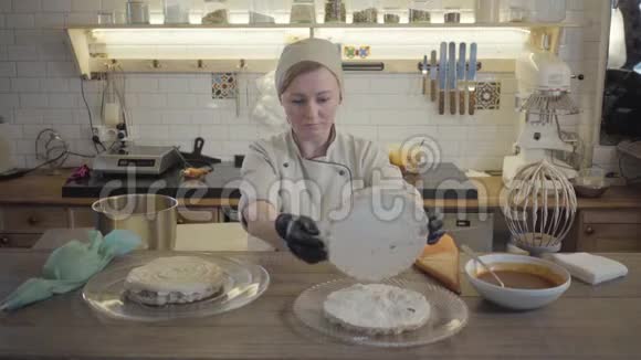 在餐厅厨房的背景上做蛋糕的女人糖果师在奶油上放第二块美味的饼干视频的预览图
