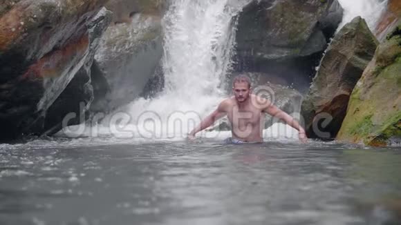 英俊的男人从热带雨林中的热带瀑布在山河里游泳在岩石河上洗澡的年轻人视频的预览图