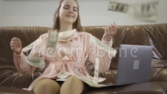 肖像可爱可爱的少女坐在笔记本电脑前的皮革沙发上一美元落在女孩身上孩子视频的预览图