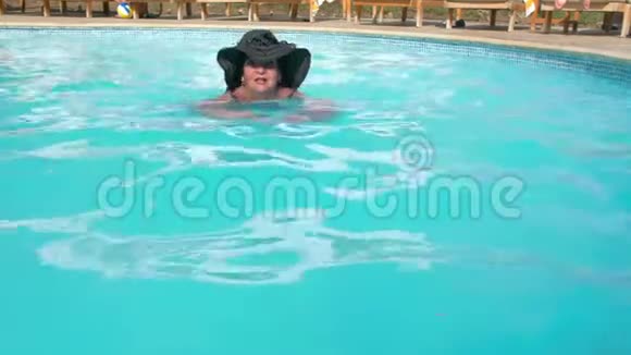 戴着帽子的白人老年女性在酒店的蓝色水池里游泳健康生活方式的概念视频的预览图