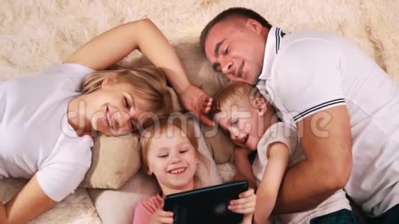 年轻的白人家庭在你休息的一天里躺在沙发上看着平板电脑视频的预览图