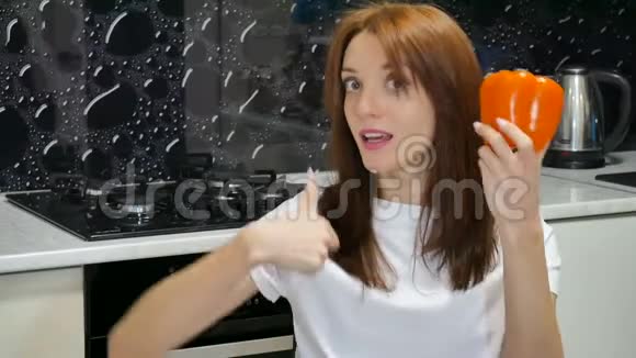 可爱的情绪激动的年轻女人带着大橙色的胡椒拇指坐在她家的厨房里视频的预览图