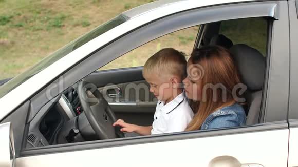 一个好奇的小男孩和他的母亲坐在汽车的车轮上慢动作视频的预览图