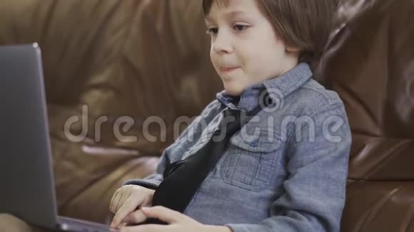 小兴奋的男孩在皮沙发上的笔记本电脑上工作视频的预览图