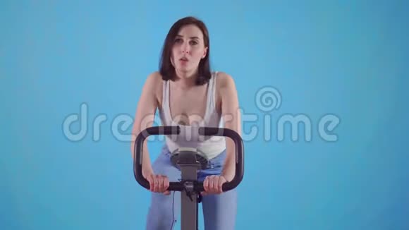年轻的运动女子骑着蓝色背景的运动自行车视频的预览图