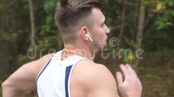 运动型运动员带着无线耳机在森林附近的小径上快速冲刺年轻强壮的运动员慢跑视频的预览图