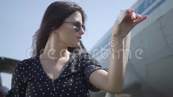 肖像可爱的年轻黑发女孩白色披肩和太阳镜在大飞机前看着相机视频的预览图
