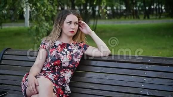 美丽的卷发女人穿着一件明亮的连衣裙躺在傍晚公园的长凳上慢动作视频的预览图