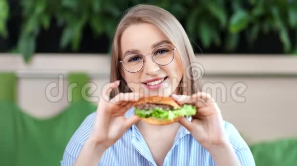 美丽的少女微笑着摆着美味可口的汉堡看镜头的画像视频的预览图