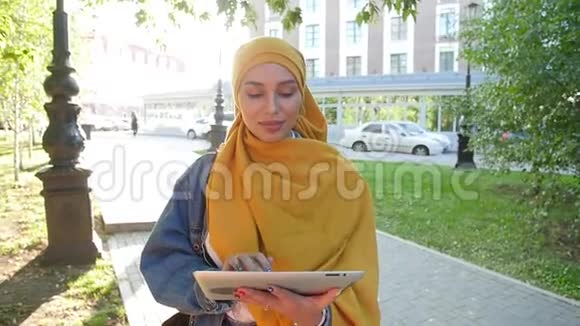戴头巾的年轻穆斯林妇女在户外用手机平板微笑视频的预览图
