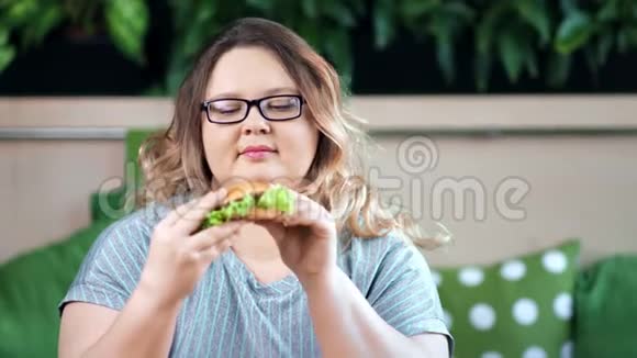 喜笑颜开的胖胖女人吃着开胃的汉堡看着镜头的画像视频的预览图