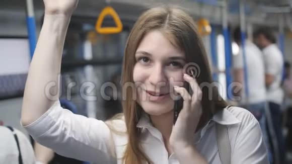 年轻快乐的乘客女人站在移动的马车里用手机说话握着一只手视频的预览图