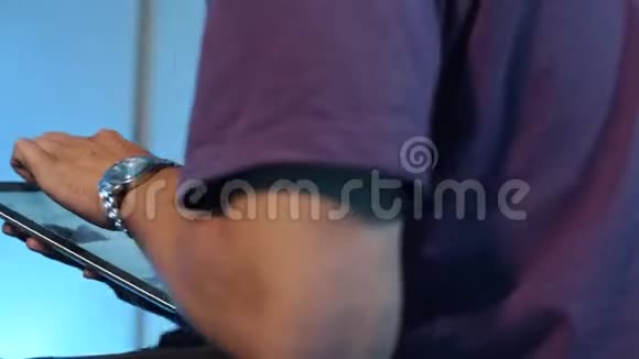 穿紫色t恤的年轻人坐在黑暗的房间里积极地使用他的平板电脑视频的预览图