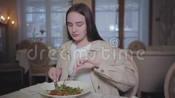 肖像可爱的年轻女子长发吃着小猪坐在餐厅的桌子旁孤独的女人视频的预览图