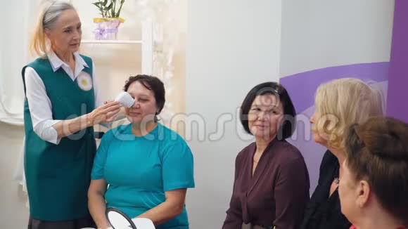 老年白发护士向老年妇女组演示硬件面部按摩视频的预览图