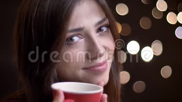 一幅年轻漂亮的白种人女性的特写肖像她喝着一杯温茶微笑着眉毛一扬看着视频的预览图