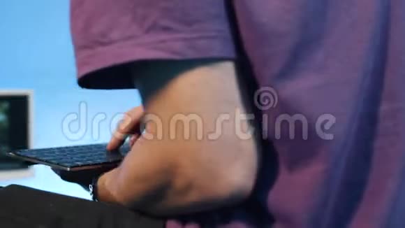 穿着t恤的男人坐在黑暗的房间里用手指切割便携式键盘视频的预览图
