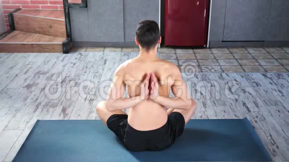健身瑜伽男双手背在背后坐在现代公寓的垫子上视频的预览图