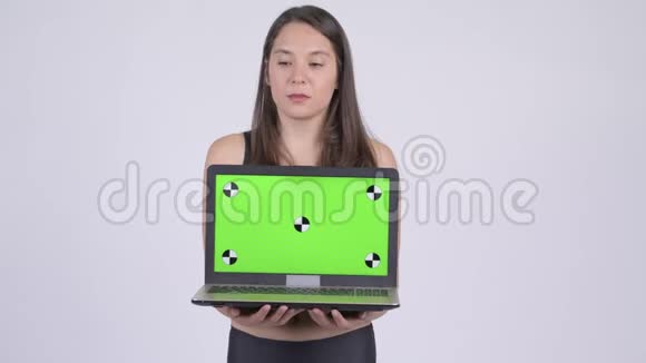 年轻快乐的多民族女性一边思考一边展示笔记本电脑准备健身房视频的预览图