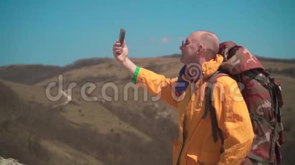 一个穿着黄色夹克和眼镜的人站在山上欣赏风景做自拍视频的预览图