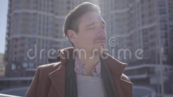 成功微笑的英俊男子的肖像穿着棕色外套站在城市街道上环顾四周高层建筑视频的预览图