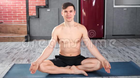 微笑运动瑜伽男子摆姿势坐在莲花的位置享受冥想看着相机视频的预览图