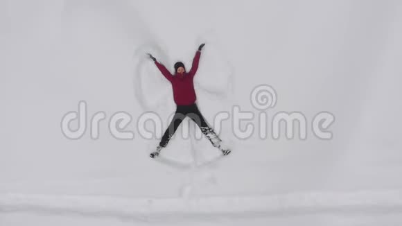 年轻女子在雪地里做一个雪天使无人驾驶的俯视图视频的预览图