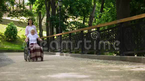 孙女把老妇人推在轮椅医院的花园里支持和照顾视频的预览图