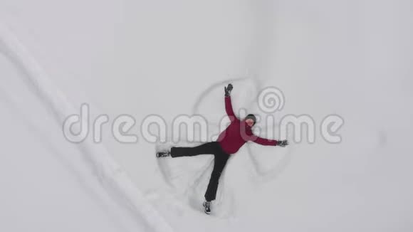 年轻女子在雪地里做一个雪天使无人驾驶的俯视图视频的预览图