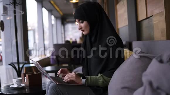 集中年轻的穆斯林妇女在咖啡馆的现代笔记本电脑上工作戴着头巾的漂亮女人拿着笔记本电脑视频的预览图
