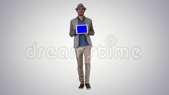 戴着帽子的闲人走着在渐变背景下向摄像机展示数字平板电脑视频的预览图
