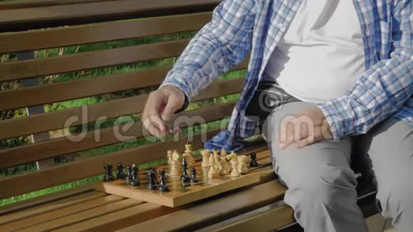 老人独自在夏天公园的长凳上下棋视频的预览图