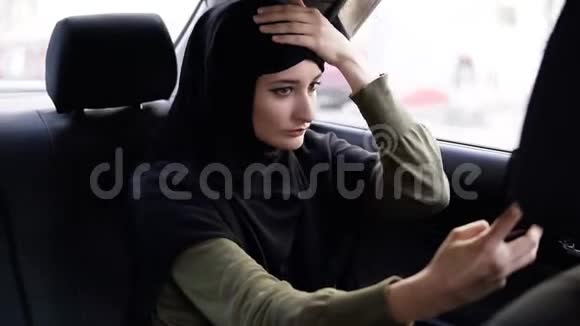 年轻有魅力的穆斯林妇女戴着头巾在车上通勤她穿着一件深色衣服坐在上面视频的预览图