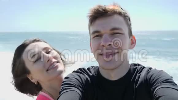 年轻快乐的微笑夫妇在岩石海滩上以自拍的方式记录自己强劲的风浪视频的预览图