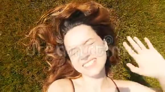 女孩躺在草地上从阳光明媚的城市挥手问好休息看着相机微笑休息日光浴视频的预览图