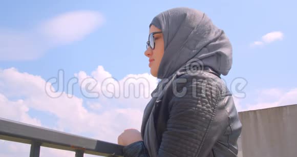 年轻漂亮的穆斯林女性戴着头巾戴着眼镜观看城市景色并转向镜头的特写镜头视频的预览图