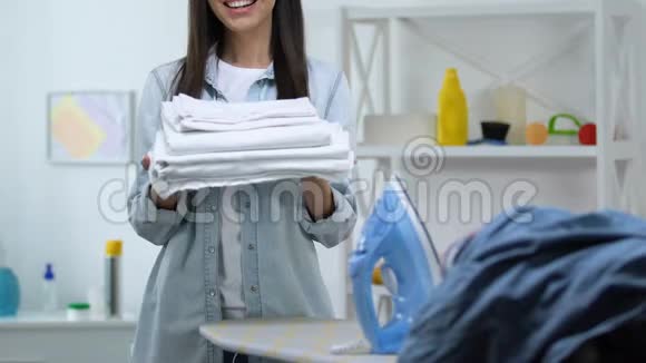 微笑的家庭主妇站在熨衣板旁拿着新鲜的亚麻布洗衣服视频的预览图