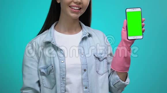 戴着手套的家庭主妇用绿色屏幕指着智能手机视频的预览图