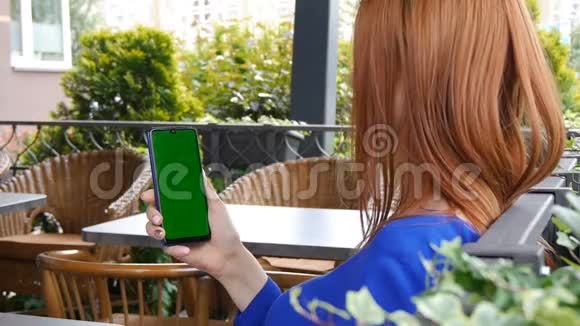 红头发的女孩坐在舒适的咖啡馆里使用带有绿色屏幕的手机视频的预览图