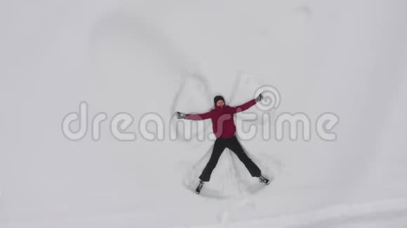 年轻女子在雪地里做雪天使无人机俯视旋转视频的预览图