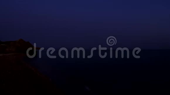 黎明海浪冲刷沙滩一个岩石悬崖突入大海天空变色视频的预览图