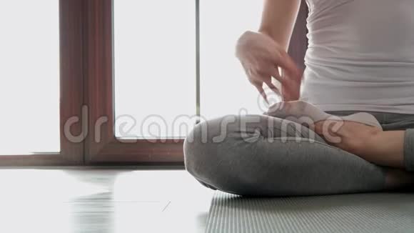 特写一个女人正坐在地板上的莲花位置家庭练习瑜伽视频的预览图