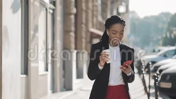 快乐的非裔美国女商人用智能手机耳机听音乐走出办公室视频的预览图