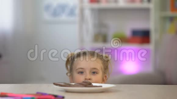 女孩子从桌上的白色盘子里偷偷吃巧克力糖过量视频的预览图