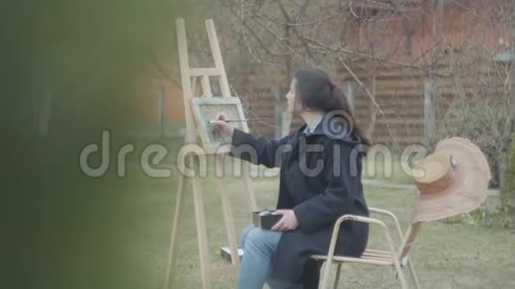 相当集中的年轻女画家坐在木制画架前画一幅画休闲女艺术家视频的预览图